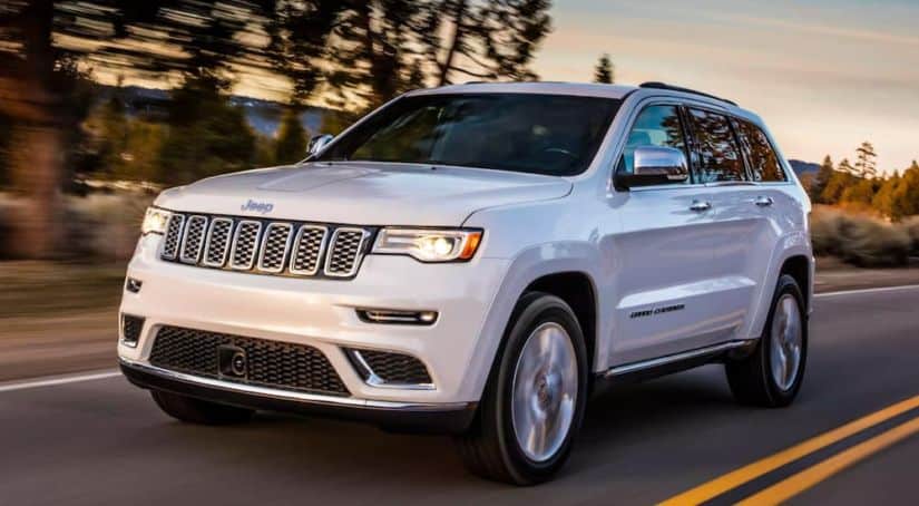 A white 2020 Jeep Grand Cherokee for sale is driving on a treelined road.