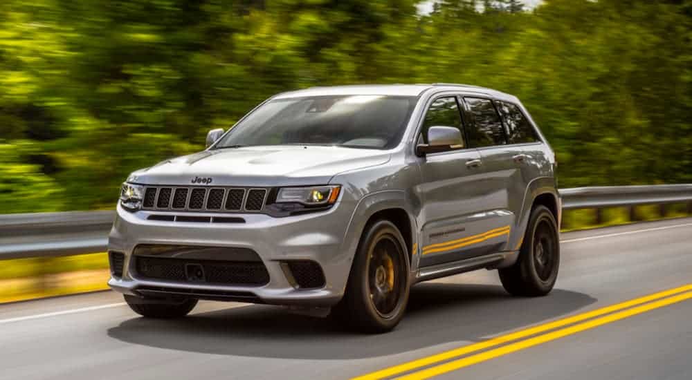 A grey 2020 Jeep Grand Cherokee Trackhawk, which is a popular Jeep for sale, is driving on a treelined road.