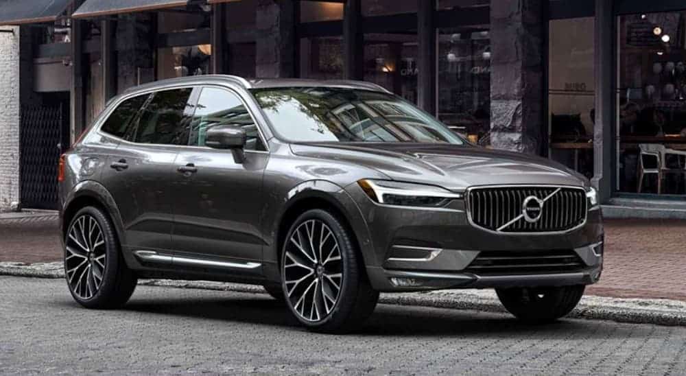 A grey 2020 Volvo XC60 is parked in front of road side stores.