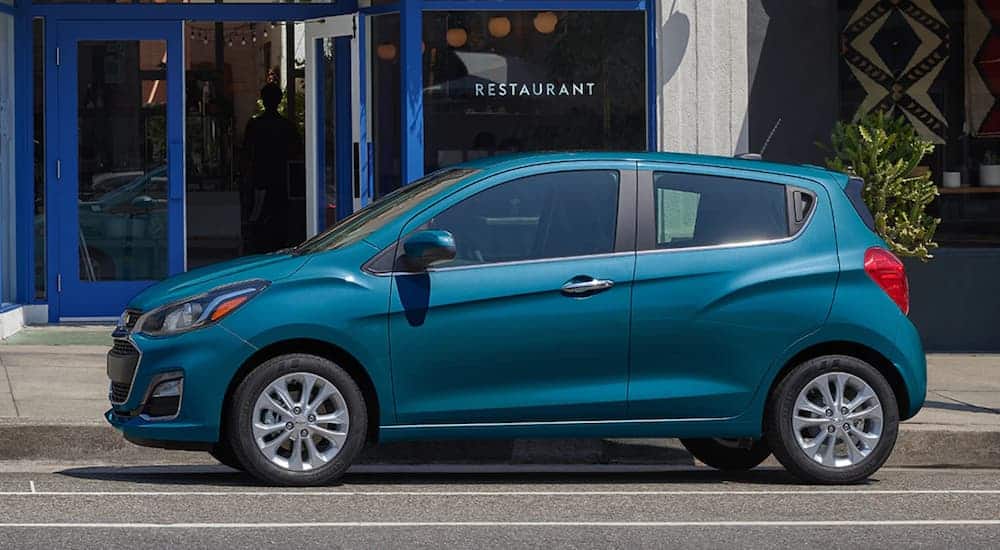 A side view of a blue 2020 Chevy spark is parked in front of a restaurant. 