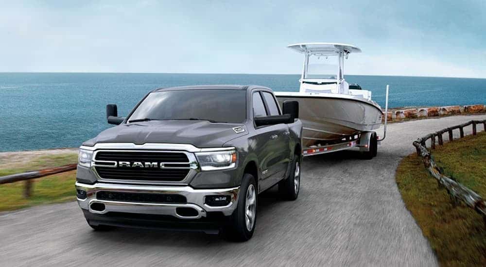 A grey 2020 Ram 1500 is towing a boat past the ocean.