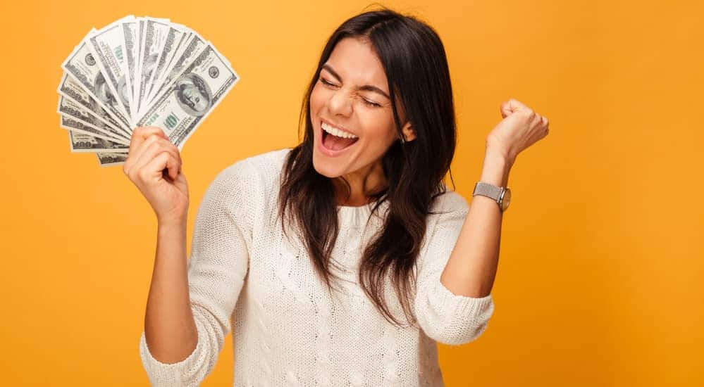 A woman is holding money while screaming in excitement about saving money. 