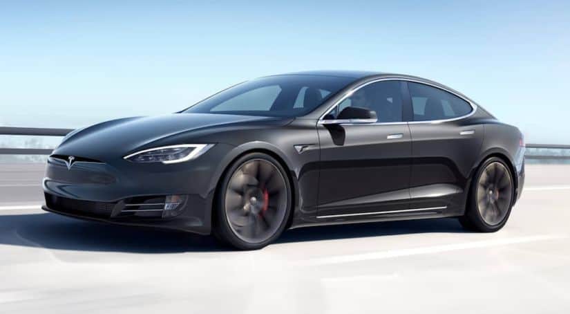 A black 2021 Tesla Model S is driving across a bridge.