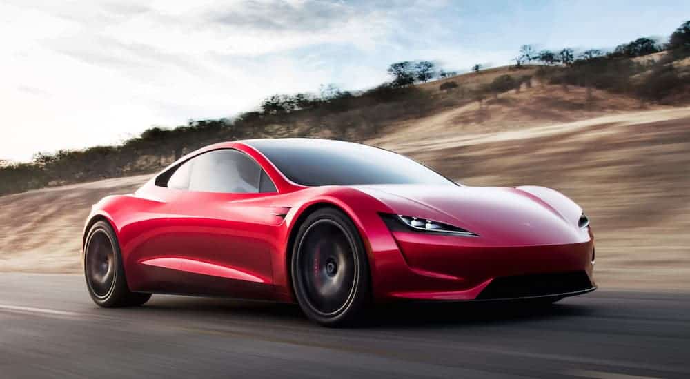 A red 2021 Tesla Roadster is speeding down the the highway past blurred hills.