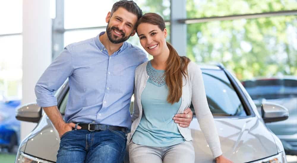 A smiling couple is standing in front of their new to them used car.