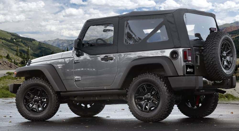 A grey 2017 Jeep Wrangler Willys Wheeler is shown from the side with mountains in the distance.