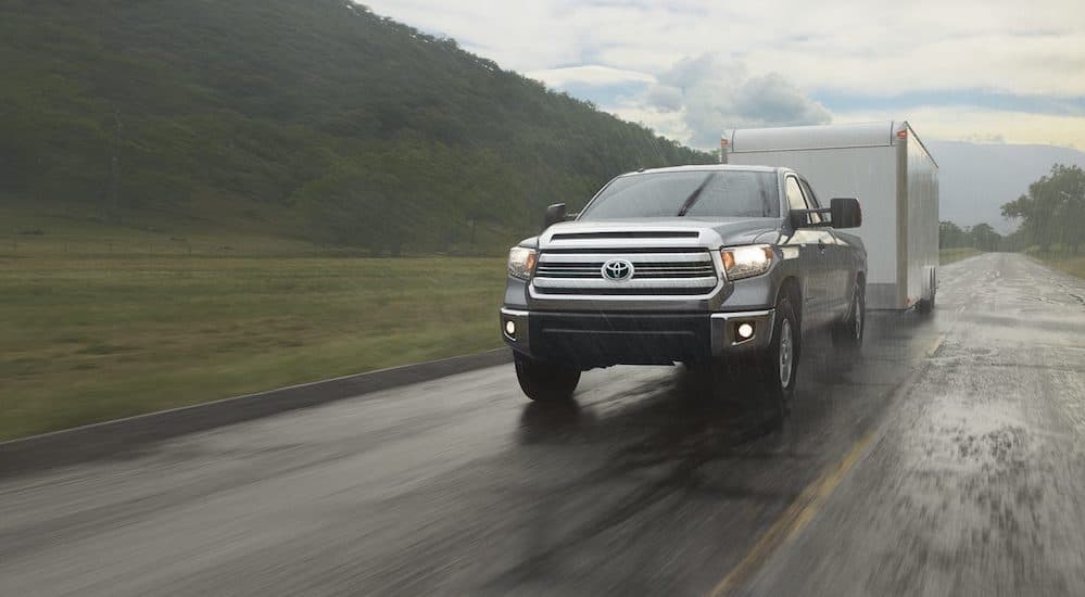 A grey 2016 Toyota Tundra is towing a large trailer on a rainy day.