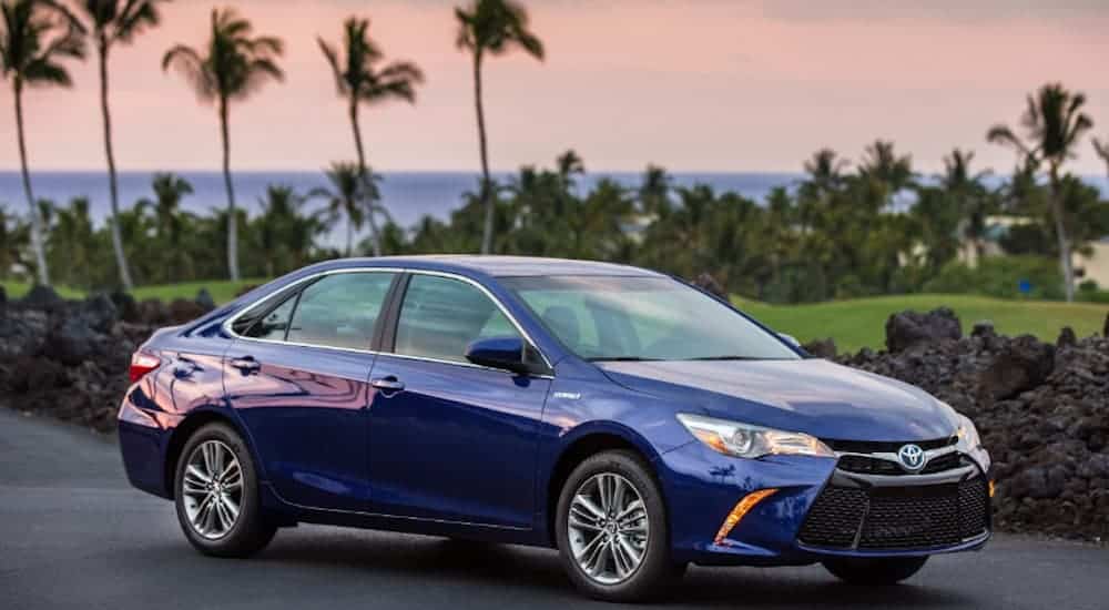 A blue 2017 Toyota Camry, which is a popular option among used cars, is parked in front of palm trees at dusk. 