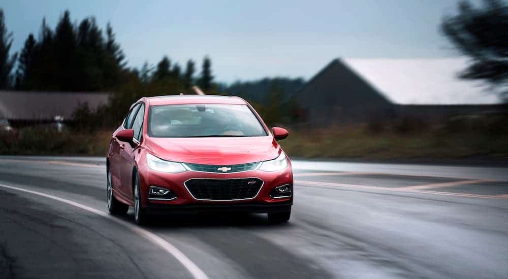 A red 2018 used Chevy Cruze is driving around a corner on a wet road.