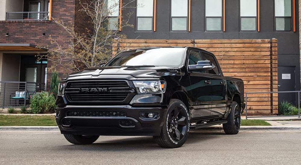 A black 2020 Ram 1500 is parked in front of a grey and wooden sided building.