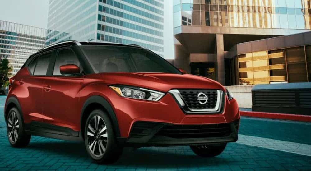 A red 2020 Nissan Kicks is parked in front of a glass office building.
