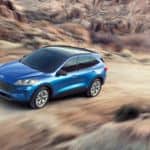 A blue 2020 Ford Escape is driving up a dirt hill with mountains in the distance.