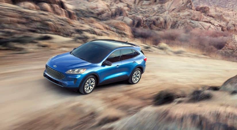 A blue 2020 Ford Escape is driving up a dirt hill with mountains in the distance.