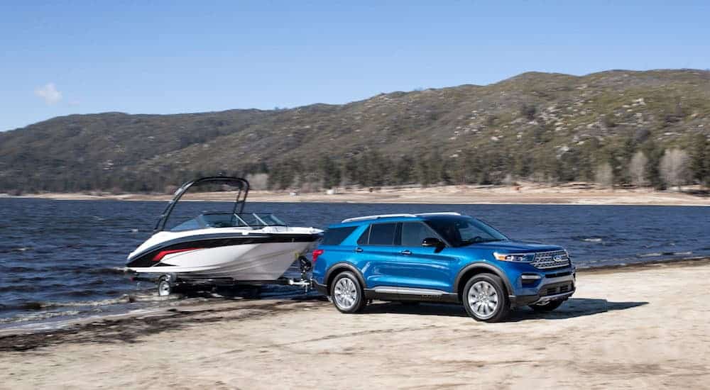 A blue 2020 Ford Explorer, which is a favorite among Ford SUVs, is towing a boat out of a lake with trees in the distance. 