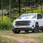 A white 2020 GMC Acadia, which wins when comparing the 2020 GMC Acadia vs 2020 Ford Explorer, is on a trail in the woods.
