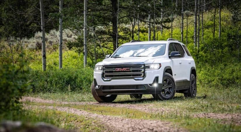 A white 2020 GMC Acadia, which wins when comparing the 2020 GMC Acadia vs 2020 Ford Explorer, is on a trail in the woods.