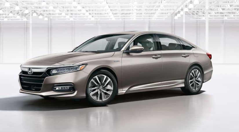 A beige 2020 Honda Accord Touring Hybrid is parked in a white showroom.
