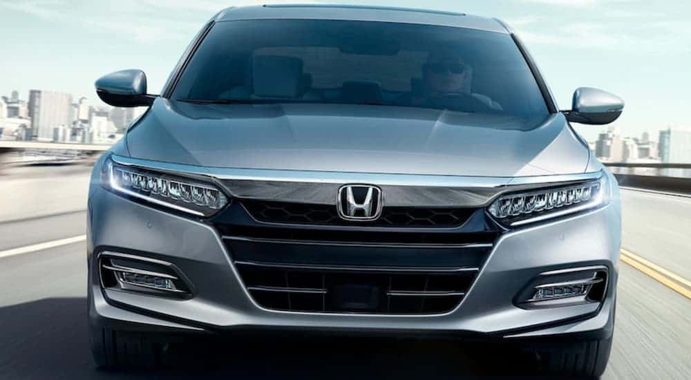 A silver 2020 Honda Accord Touring is driving on a city highway and shown from the front.