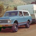A blue 1969 Chevy K5 Blazer, which is one of the classic Chevy SUVs, is towing a camper.