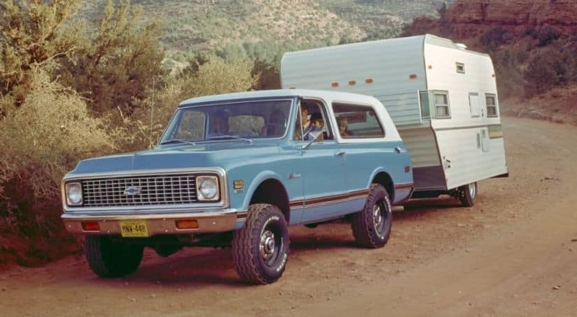 A blue 1969 Chevy K5 Blazer, which is one of the classic Chevy SUVs, is towing a camper.