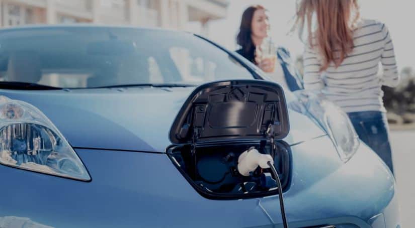 A blue electric vehicle, a popular topic in current auto news, is charging in front of two women.