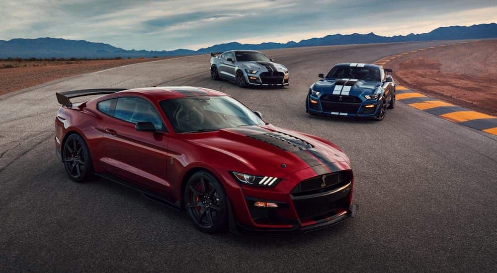 A red 2020 Ford Mustang GT500 is in front of a blue one and a silver one in the desert.