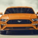 An orange 2020 Ford Mustang is doing a burnout after leaving a Ford dealership.