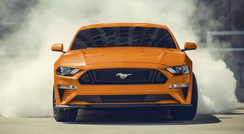 An orange 2020 Ford Mustang is doing a burnout after leaving a Ford dealership.