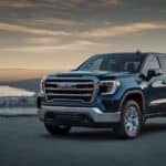 A blue 2020 GMC Sierra 1500 is parked in front of a river at sunset.