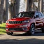 A red 2020 Jeep Grand Cherokee is driving on a tree-lined road.