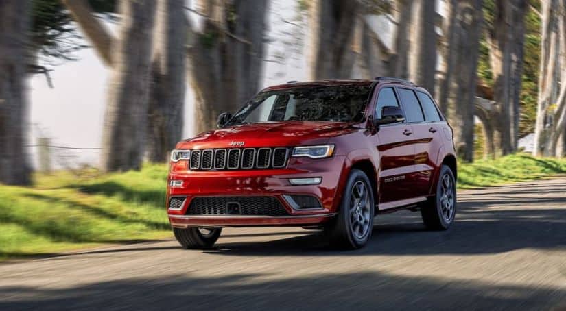 A red 2020 Jeep Grand Cherokee is driving on a tree-lined road.