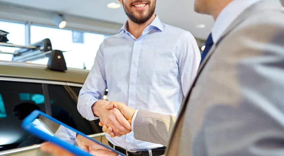 A smiling car salesman is shaking the hand of a smiling customer. 