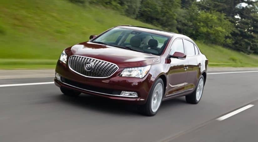 A burgundy 2016 Buick LaCrosse is driving on a grass-lined highway.