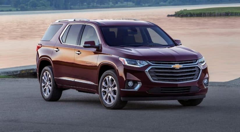 A burgundy 2018 used Chevy Traverse is parked in front of a lake at sunset.