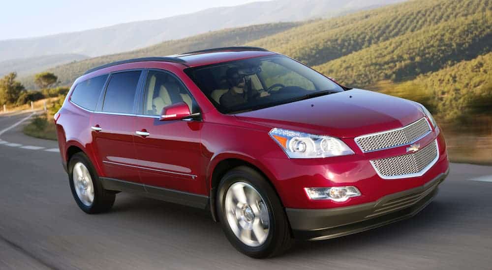 A red 2009 used Chevy Traverse is driving pasts fields in the hills.