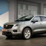A silver 2020 Cadillac XT5 is driving in front of a warehouse and wins when comparing the 2020 Cadillac XT5 vs 2020 BMW X3.