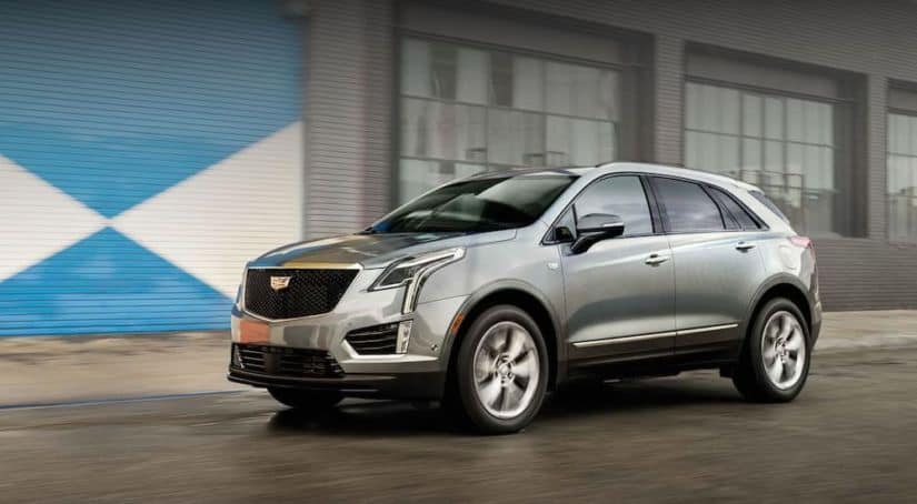 A silver 2020 Cadillac XT5 is driving in front of a warehouse and wins when comparing the 2020 Cadillac XT5 vs 2020 BMW X3.