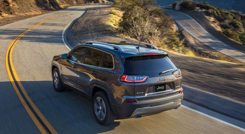 A dark grey 2020 Jeep Cherokee is driving on a winding mountain road.