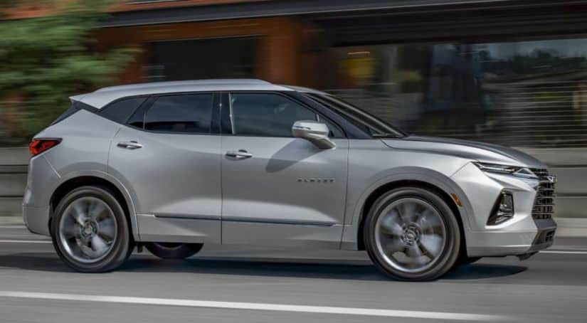 A silver 2020 Chevy Blazer, which wins when comparing the 2020 Chevy Blazer vs 2020 Jeep Cherokee, is driving past blurred buildings.