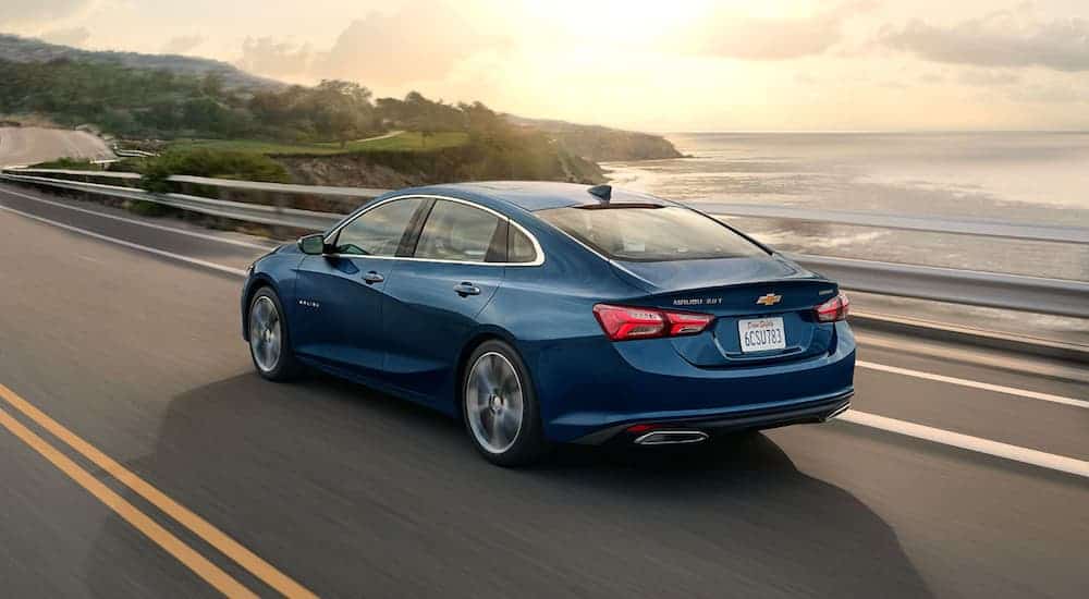 A blue 2020 Chevy Malibu is driving past the ocean at sun set.