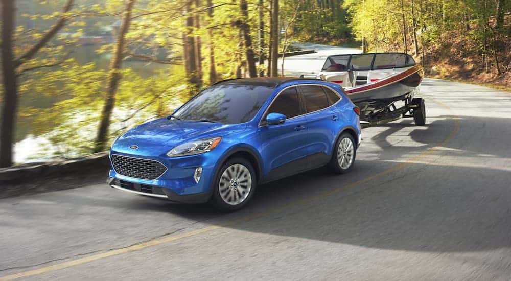 A blue 2020 Ford Escape is towing a boat past a lake and trees.
