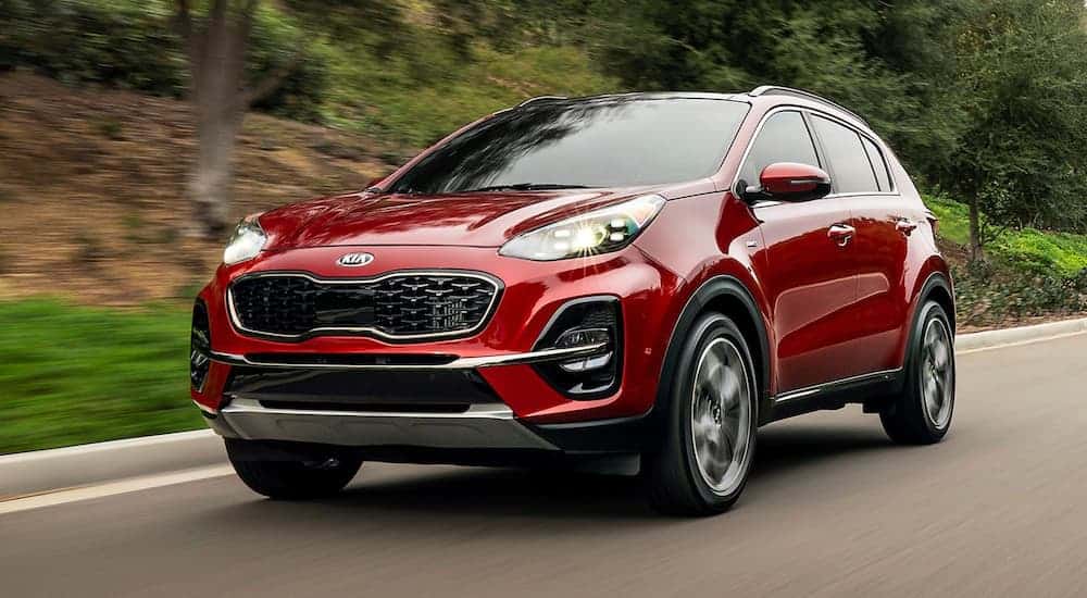 A red 2020 Kia Sportage is driving past trees.