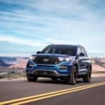 A blue 2020 Ford Explorer, which wins when comparing the 2020 Ford Explorer vs 2020 Toyota Highlander, is driving on a highway with mountains in the distance.