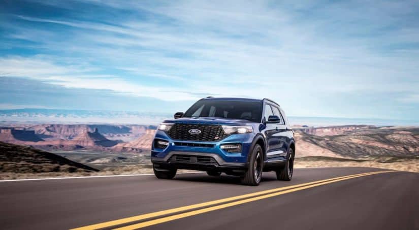 A blue 2020 Ford Explorer, which wins when comparing the 2020 Ford Explorer vs 2020 Toyota Highlander, is driving on a highway with mountains in the distance.