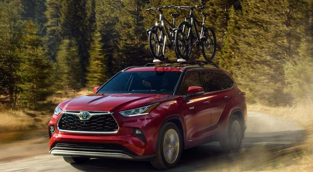 A red 2020 Toyota Highlander is driving on a dirt path with bikes on its roof rack.