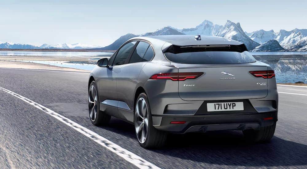 A grey 2020 Jaguar I-Pace Electric SUV is driving on a road with mountains in the distance.