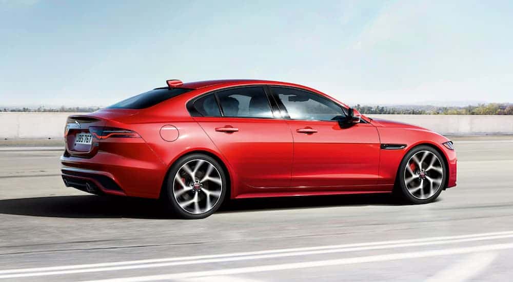 A red 2020 Jaguar XE Sedan is driving on a highway with blue skies.