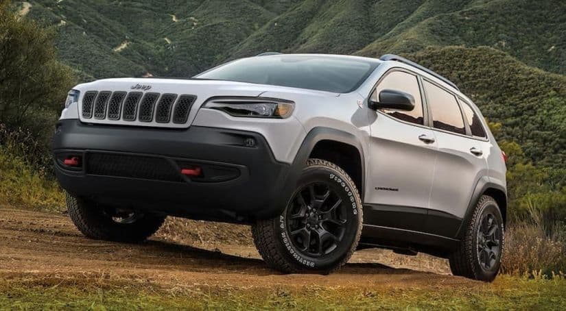 A silver 2020 Jeep Cherokee Trailhawk is driving up a dirt hill.