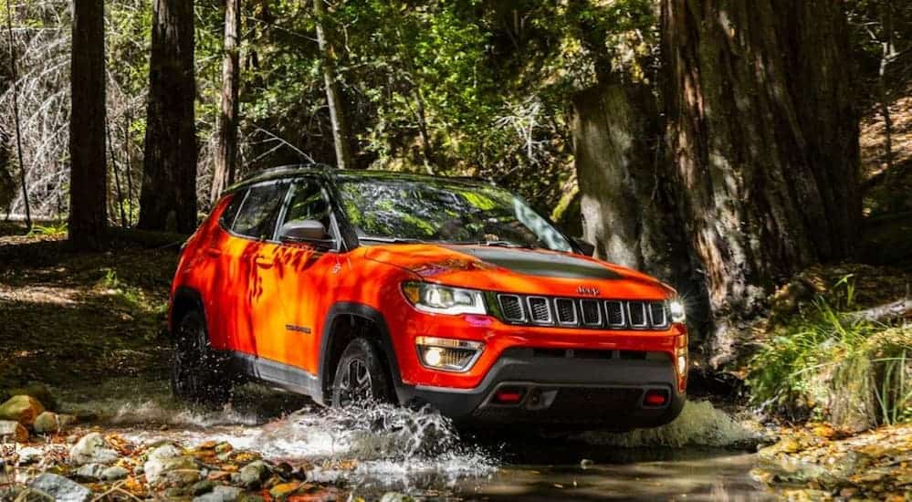 A red 2020 Jeep Compass Trailhawk is driving through the woods on a dirt trail.