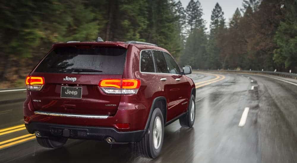 A burgundy 2020 Jeep Grand Cherokee is driving in the rain.